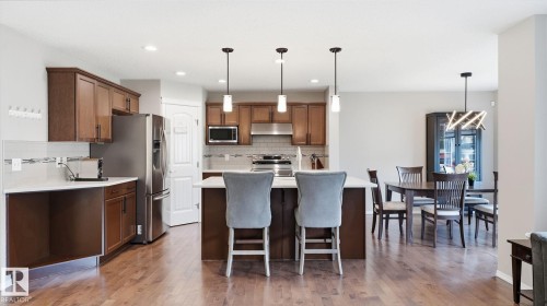 Wood-finish flooring throughout, kitchen with dark wood cabinetry, stainless steel appliances, white countertops, and a subway tile backsplash - 4610 Westcliff Point(E) Sw, Edmonton, AB 