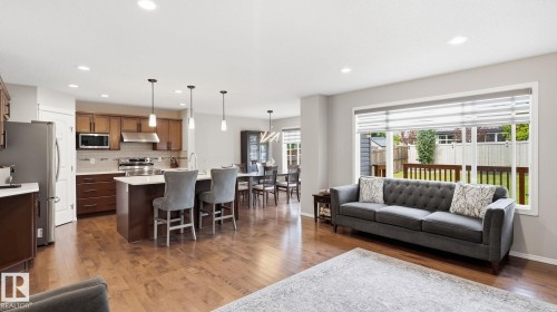Open-concept living space featuring wood-finish flooring, recessed lighting, a kitchen island with pendant lighting, and a large window overlooking the backyard - 4610 Westcliff Point(E) Sw, Edmonton, AB 