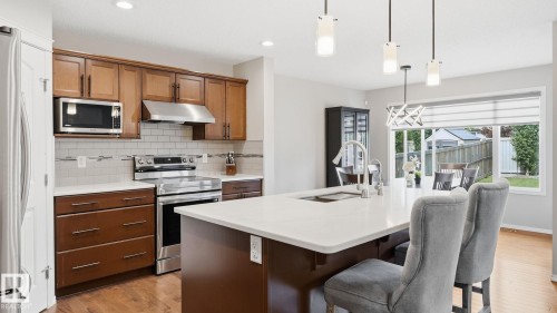 Kitchen featuring wood-finish cabinetry, stainless steel appliances, white subway tile backsplash, and a large central island with a white countertop - 4610 Westcliff Point(E) Sw, Edmonton, AB 