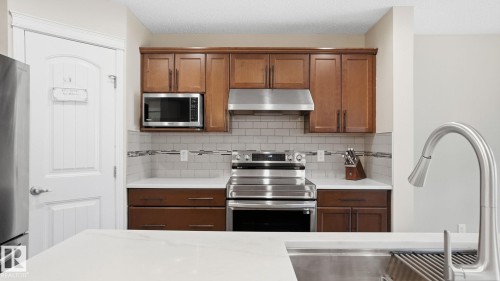 Kitchen featuring wood-finish cabinetry, stainless steel appliances, white subway tile backsplash with decorative accent, and white countertops - 4610 Westcliff Point(E) Sw, Edmonton, AB 