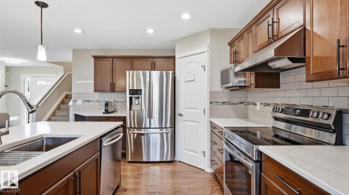 Kitchen featuring wood-finish flooring, stainless steel appliances, white subway tile backsplash, white countertops, and wood cabinetry - 4610 Westcliff Point(E) Sw, Edmonton, AB 
