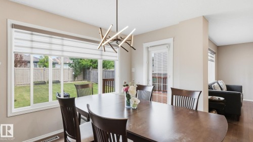 Expansive rear window overlooking a fenced backyard, contemporary chandelier, wood-finish flooring, and a private back deck - 4610 Westcliff Point(E) Sw, Edmonton, AB 
