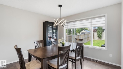 Spacious dining area featuring wood-finish flooring, a contemporary chandelier, a built-in display cabinet, and a large window - 4610 Westcliff Point(E) Sw, Edmonton, AB 