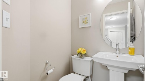 Pedestal sink with a polished chrome faucet, toilet with a white tank and bowl, and a circular wall-mounted mirror - 4610 Westcliff Point(E) Sw, Edmonton, AB 