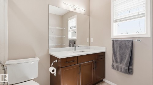 Bathroom featuring a wood-finish vanity with a white countertop, an integrated sink, a rectangular mirror, and a window with blinds - 4610 Westcliff Point(E) Sw, Edmonton, AB 