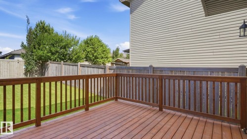 Spacious wood-finish deck with a wood railing, leading to a fenced backyard with a manicured lawn - 4610 Westcliff Point(E) Sw, Edmonton, AB 