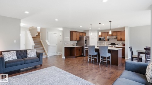 Open-concept living space with wood-finish flooring, a kitchen island with pendant lighting, stainless steel appliances, and wood cabinetry - 4610 Westcliff Point(E) Sw, Edmonton, AB 