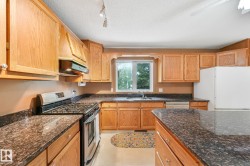 Kitchen featuring light wood cabinetry, dark speckled countertops, and a stainless steel gas range with overhead ventilation - 