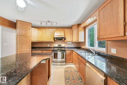 Kitchen featuring an expansive granite-finish island and countertops, wood-finish cabinetry, stainless steel appliances, and a window above the sink - 5502 45 Street, Stony Plain, AB - Indoor Photo Showing Kitchen With Double Sink
