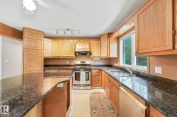 Kitchen featuring an expansive granite-finish island and countertops, wood-finish cabinetry, stainless steel appliances, and a window above the sink - 