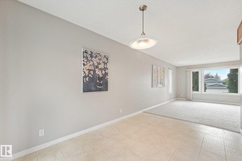 Open-concept living area featuring a large picture window, an additional vertical window, and a contemporary pendant light fixture - 5502 45 Street, Stony Plain, AB - Indoor Photo Showing Other Room