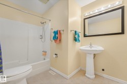 Bathroom featuring a pedestal sink, framed mirror with vanity lighting, and a white bathtub with an integrated shower and white surround - 
