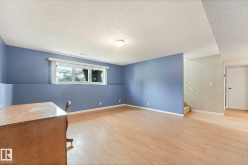 Finished basement area featuring wood-finish flooring, a double window with white blinds, and a partial staircase - 5502 45 Street, Stony Plain, AB - Indoor Photo Showing Other Room