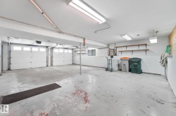 Two-car garage featuring automatic overhead doors with frosted glass panels, concrete flooring, exposed overhead fluorescent lighting, and built-in shelving - 