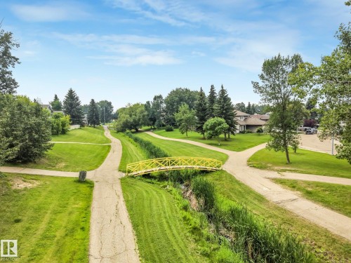 Expansive green space featuring multiple walking paths, a distinctive yellow pedestrian bridge, mature trees, and a natural drainage channel - 5502 45 Street, Stony Plain, AB - Outdoor With View