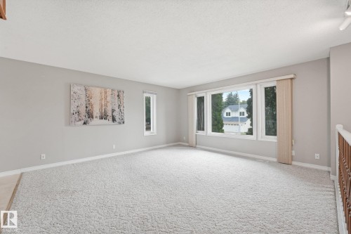 Spacious living area featuring light gray wall paint, white textured ceilings, and light-toned carpeting - 5502 45 Street, Stony Plain, AB - Indoor