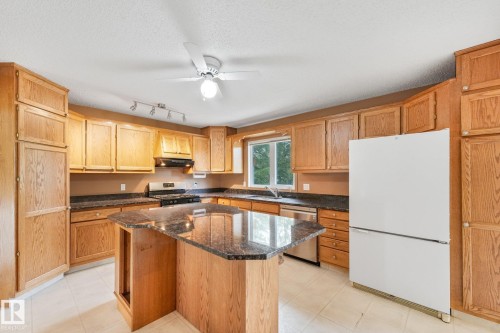 Kitchen featuring extensive wood cabinetry, a central island with a stone-finish countertop, stainless steel dishwasher, and a window above the sink - 5502 45 Street, Stony Plain, AB - Indoor Photo Showing Kitchen