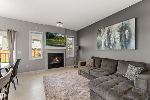 Living area featuring a tiled fireplace with a mantel, light wood-finish flooring, and multiple windows - 12218 176 Avenue Nw, Edmonton, AB 
