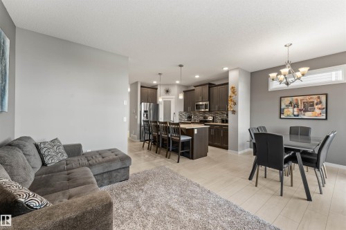 Open-concept living space featuring wood-finish flooring, a kitchen island with seating, dark wood cabinetry, stainless steel appliances, and a dining area with a chandelier - 12218 176 Avenue Nw, Edmonton, AB 