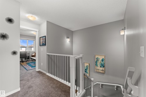 Carpeted hallway featuring a white spindle railing and wall-mounted sconces - 12218 176 Avenue Nw, Edmonton, AB 