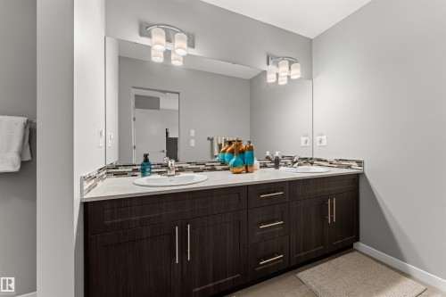 Dual vanity featuring integrated sinks, a continuous mirror, and under-cabinet storage with contemporary hardware - 12218 176 Avenue Nw, Edmonton, AB 