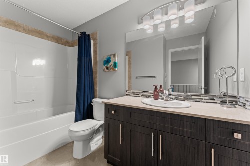 White bathtub with tiled surround, dark wood-finish vanity with an undermount sink, solid surface countertop, and mosaic tile backsplash - 12218 176 Avenue Nw, Edmonton, AB 
