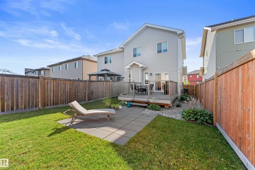Expansive backyard featuring a manicured lawn, a large wooden deck with railing, and a stone paver patio - 12218 176 Avenue Nw, Edmonton, AB 