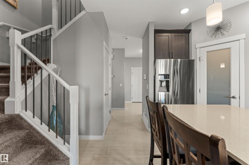 Hardwood-style flooring, stainless steel refrigerator, white staircase with wrought iron spindles, built-in cabinetry, and a frosted glass door - 12218 176 Avenue Nw, Edmonton, AB 