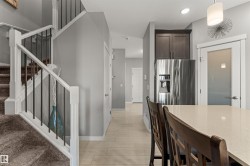 Hardwood-style flooring, stainless steel refrigerator, white staircase with wrought iron spindles, built-in cabinetry, and a frosted glass door - 