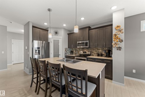Kitchen featuring a central island with dual sinks, stainless steel appliances, dark wood-finish cabinetry, and mosaic tile backsplash - 12218 176 Avenue Nw, Edmonton, AB 
