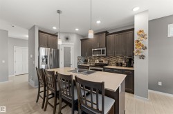 Kitchen featuring a central island with dual sinks, stainless steel appliances, dark wood-finish cabinetry, and mosaic tile backsplash - 