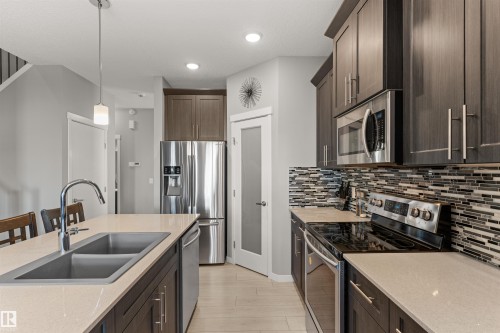 Modern kitchen featuring stainless steel appliances, dark wood-finish cabinetry, light countertops, a dual basin sink, and a tiled backsplash - 12218 176 Avenue Nw, Edmonton, AB 