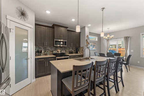 Kitchen featuring dark wood-finish cabinetry, stainless steel appliances, a mosaic tile backsplash, and a large island with a light-toned countertop - 12218 176 Avenue Nw, Edmonton, AB 