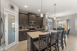 Kitchen featuring dark wood-finish cabinetry, stainless steel appliances, a mosaic tile backsplash, and a large island with a light-toned countertop - 