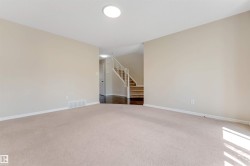 Carpeted living area with light-toned walls, recessed ceiling lighting, and a staircase featuring wood-finish treads and white risers - 