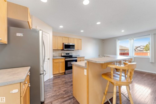 Kitchen featuring wood-finish flooring, recessed ceiling lights, light wood cabinetry, stainless steel appliances, and a breakfast bar with stone-finish countertop - 1124 37A Avenue Nw, Edmonton, AB 