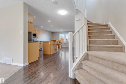 Carpeted staircase with white railings, wood-finish flooring, recessed lighting, light-toned cabinetry, and a kitchen island with a raised breakfast bar - 1124 37A Avenue Nw, Edmonton, AB 
