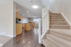 Carpeted staircase with white railings, wood-finish flooring, recessed lighting, light-toned cabinetry, and a kitchen island with a raised breakfast bar - 