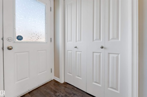 White entry door with decorative glass, wood-finish flooring, and white bifold closet doors - 1124 37A Avenue Nw, Edmonton, AB 