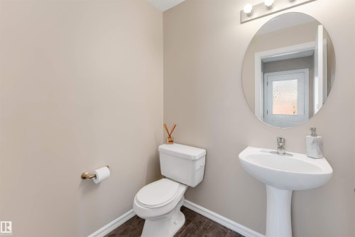 Pedestal sink with chrome faucet, oval mirror, wall-mounted light fixture, white toilet, and wood-finish flooring - 1124 37A Avenue Nw, Edmonton, AB 