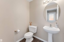 Pedestal sink with chrome faucet, oval mirror, wall-mounted light fixture, white toilet, and wood-finish flooring - 