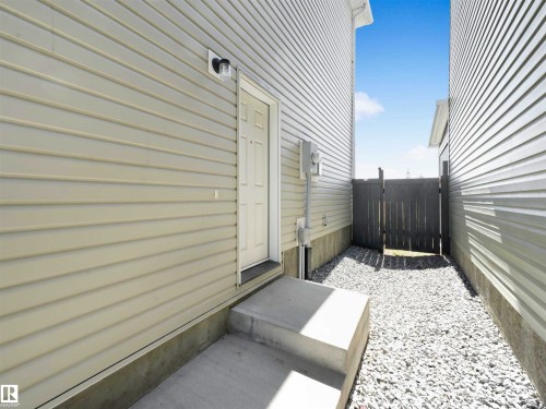 Siding exterior with a concrete stoop, leading to a gravel pathway with a wooden gate - 2435 12 Avenue Nw, Edmonton, AB 