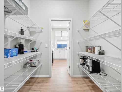 Pantry with extensive wire shelving, wood-finish flooring, and a doorway opening to a kitchen with white cabinetry - 2435 12 Avenue Nw, Edmonton, AB 