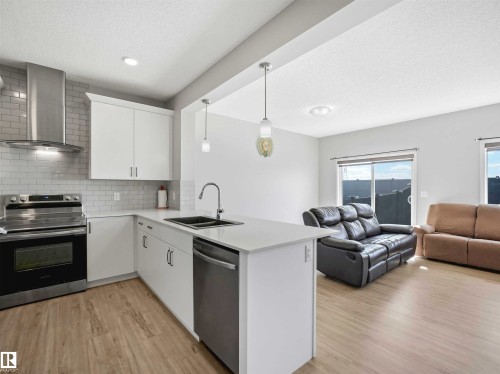 Kitchen featuring white cabinetry, subway tile backsplash, stainless steel appliances, and wood-finish flooring - 2435 12 Avenue Nw, Edmonton, AB 