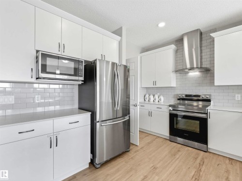 White cabinetry, subway tile backsplash, stainless steel appliances, wood-finish flooring, and white countertops - 2435 12 Avenue Nw, Edmonton, AB 
