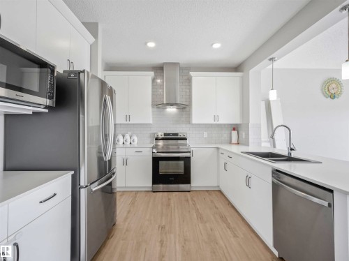 White cabinetry with brushed nickel hardware, stainless steel appliances, light wood-finish flooring, white countertop, and subway tile backsplash - 2435 12 Avenue Nw, Edmonton, AB 