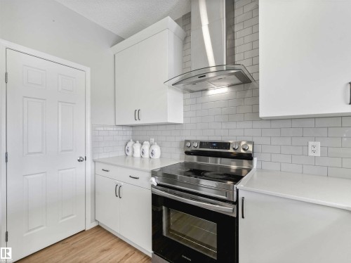 White cabinetry, white countertops, stainless steel range, stainless steel range hood, and subway tile backsplash - 2435 12 Avenue Nw, Edmonton, AB 