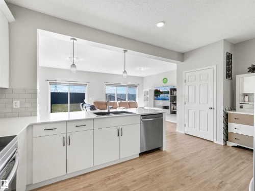 White kitchen cabinetry with stainless steel appliances, a white subway tile backsplash, and wood-finish flooring - 2435 12 Avenue Nw, Edmonton, AB 