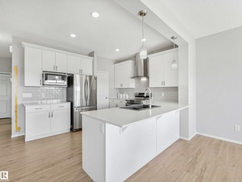 Modern kitchen featuring light wood-finish flooring, white cabinetry, stainless steel appliances, a white subway tile backsplash, and a large island with an undermount sink - 2435 12 Avenue Nw, Edmonton, AB 