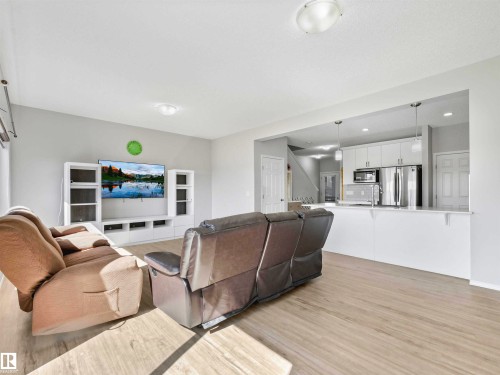 Wood-finish flooring throughout, with a recessed kitchen featuring white cabinetry and stainless steel appliances - 2435 12 Avenue Nw, Edmonton, AB 